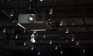 A black projector mounted on the ceiling of a dark room